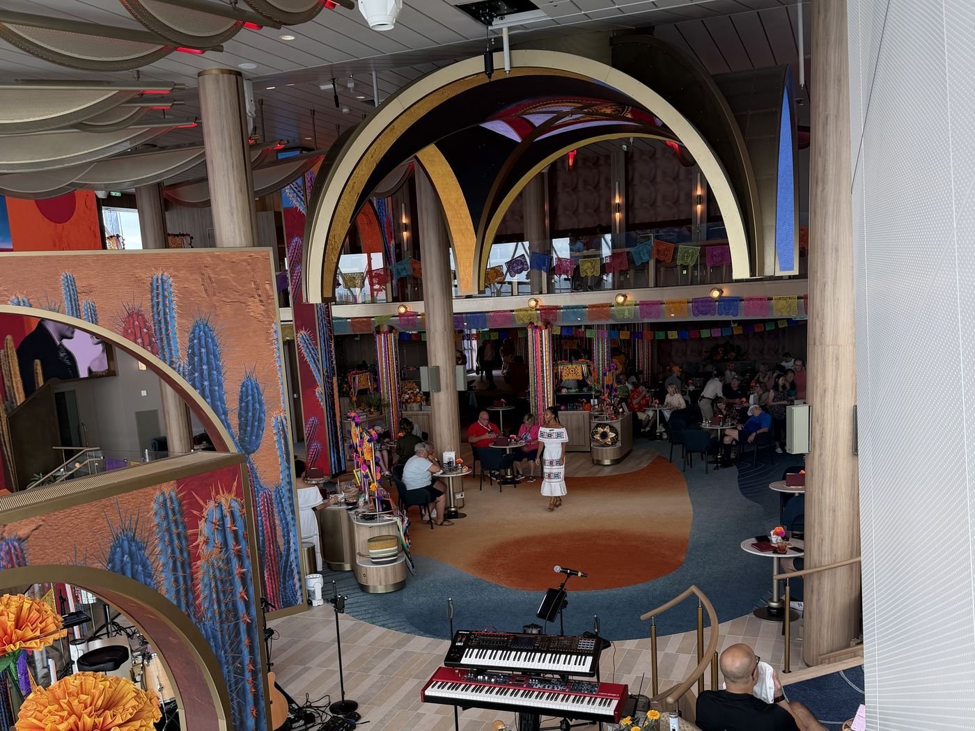 The Bazaar aboard Celebrity Xcel during a Mexican festival, gold arches and papel picado banners over a live music stage