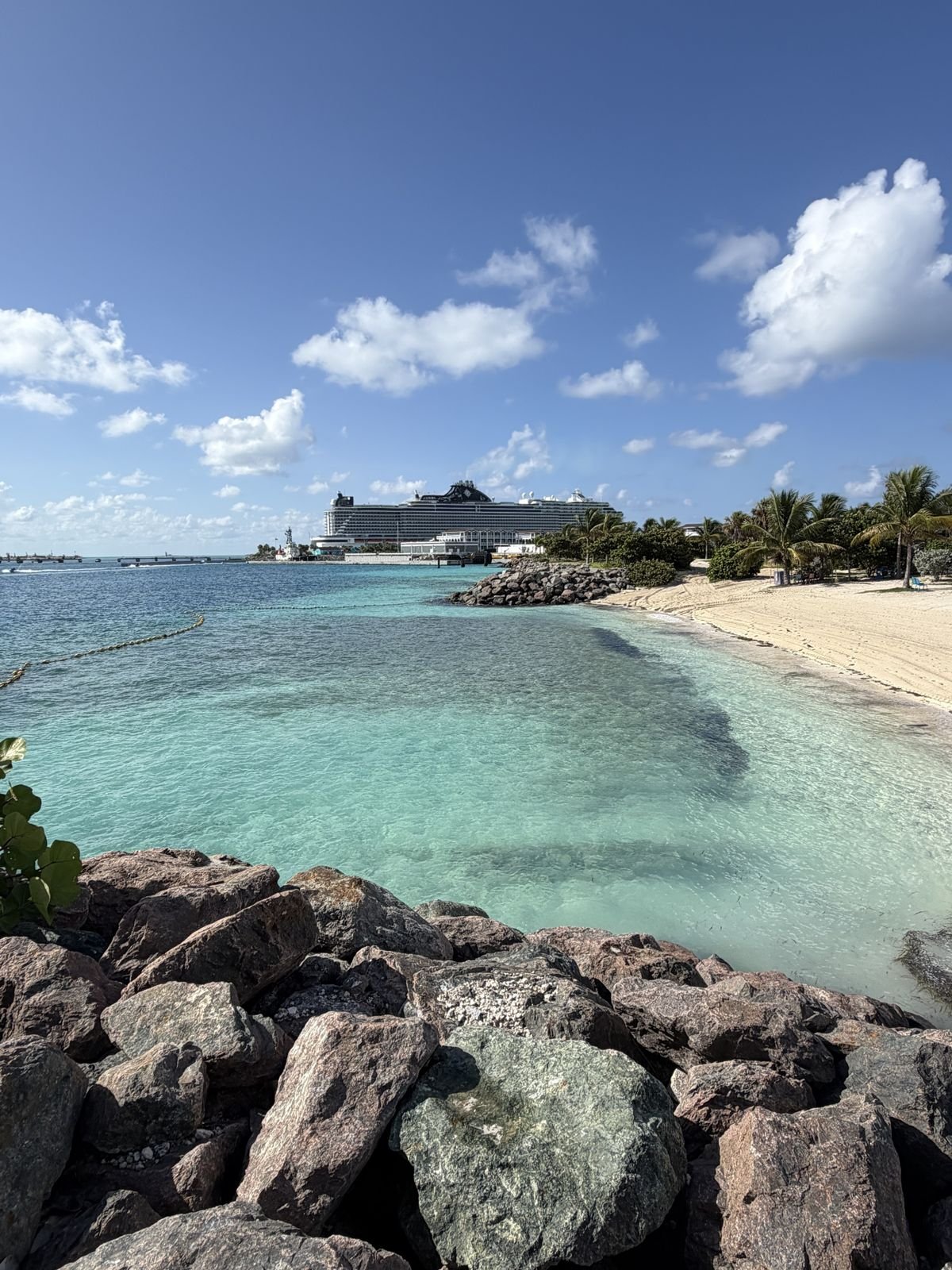 A clear, shallow lagoon and white sand beach with a cruise ship in the distance