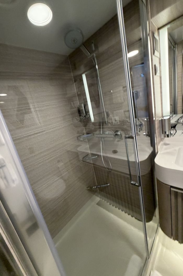 A walk-in shower behind a glass door, with a rain head, a handheld wand and wall-mounted soap dispensers.