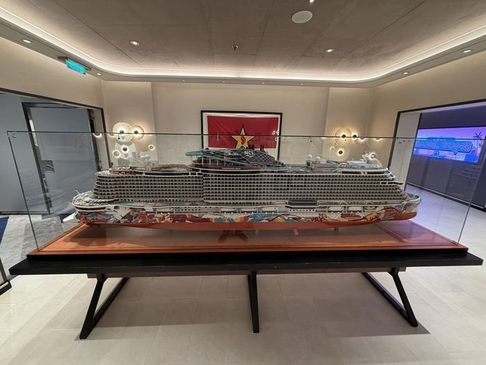 A large, detailed scale model of Norwegian Aqua in a glass case on a wooden plinth, her hull painted in a colorful mural, in a softly lit room on board.