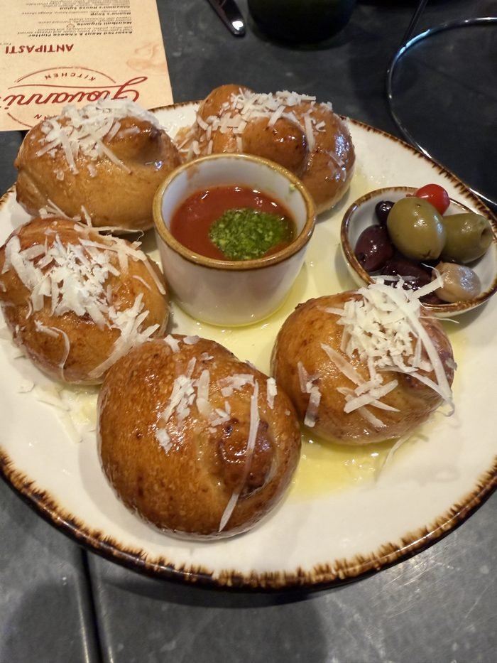 Golden bread knots with grated cheese, red dipping sauce and olives at Giovanni's Kitchen.