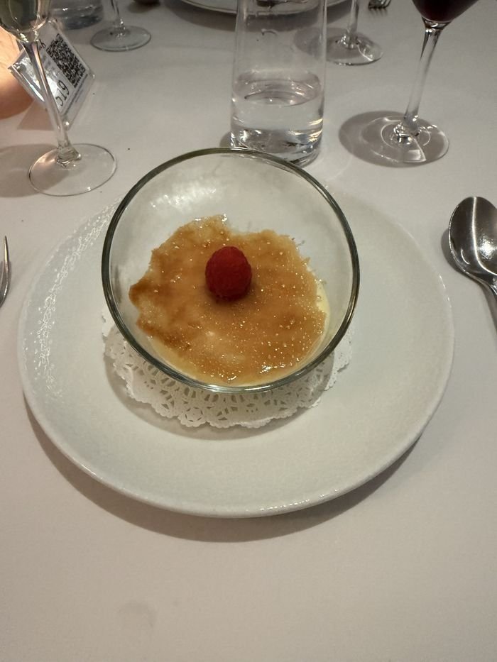 Île Flottante in a glass dish under a crackled caramelized sugar top, with a single raspberry.
