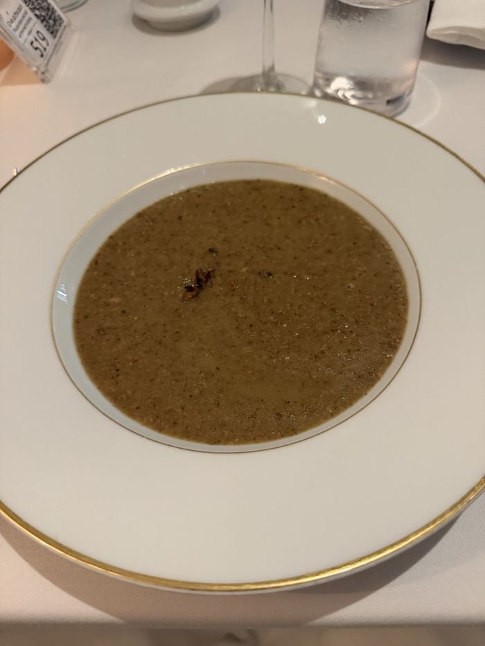 A wide gold-rimmed bowl of smooth, speckled mushroom soup.