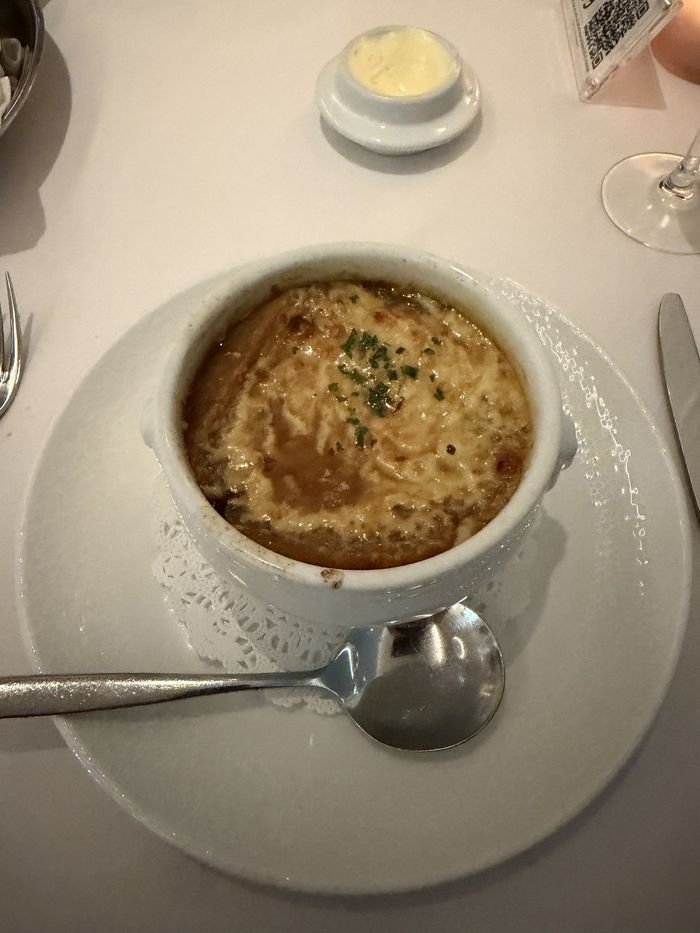 A crock of French onion soup under melted, browned cheese, with butter on the side.