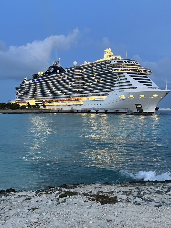 MSC Seashore lit up at dusk alongside the pier at Ocean Cay, seen across the water from the island's rocky shore
