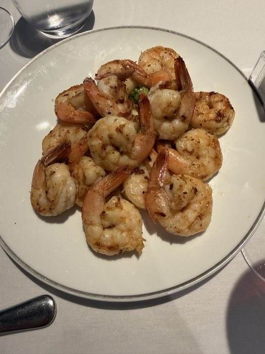 A ring of large grilled shrimp with tails on, arranged around a small mound of broccoli on a white plate in the Yacht Club restaurant