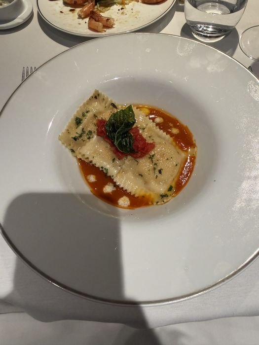 Two large ravioli in a tomato sauce, topped with fresh basil and diced tomato, with small white cheese dots around the bowl