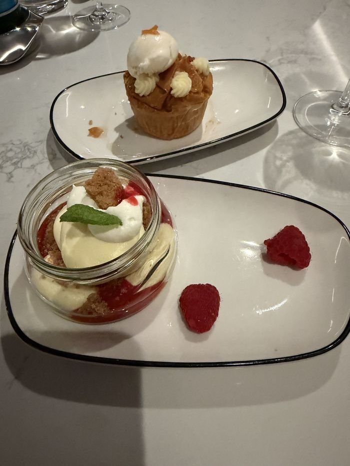 Two desserts on white plates: a vanilla cheesecake layered with raspberry in a small glass jar, and behind it a golden pastry topped with a scoop of sorbet.