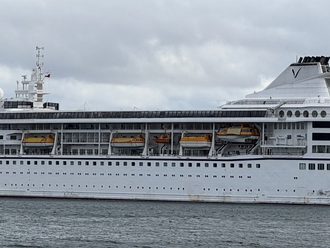 Villa Vie Odyssey, a white cruise ship with a navy hull stripe and orange lifeboats, alongside a pier under an overcast sky