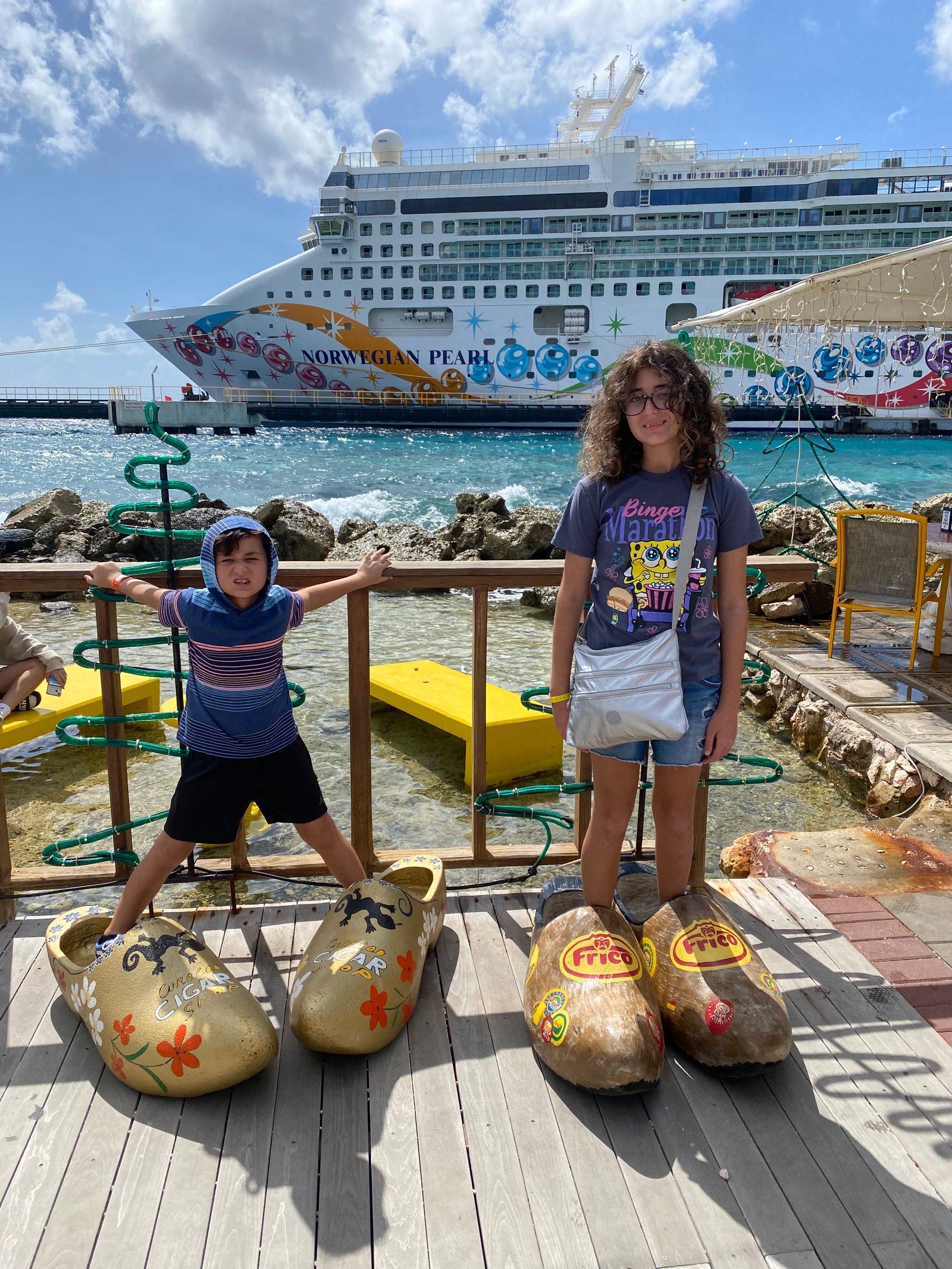 Two kids posing at port with the Norwegian Pearl docked behind them.